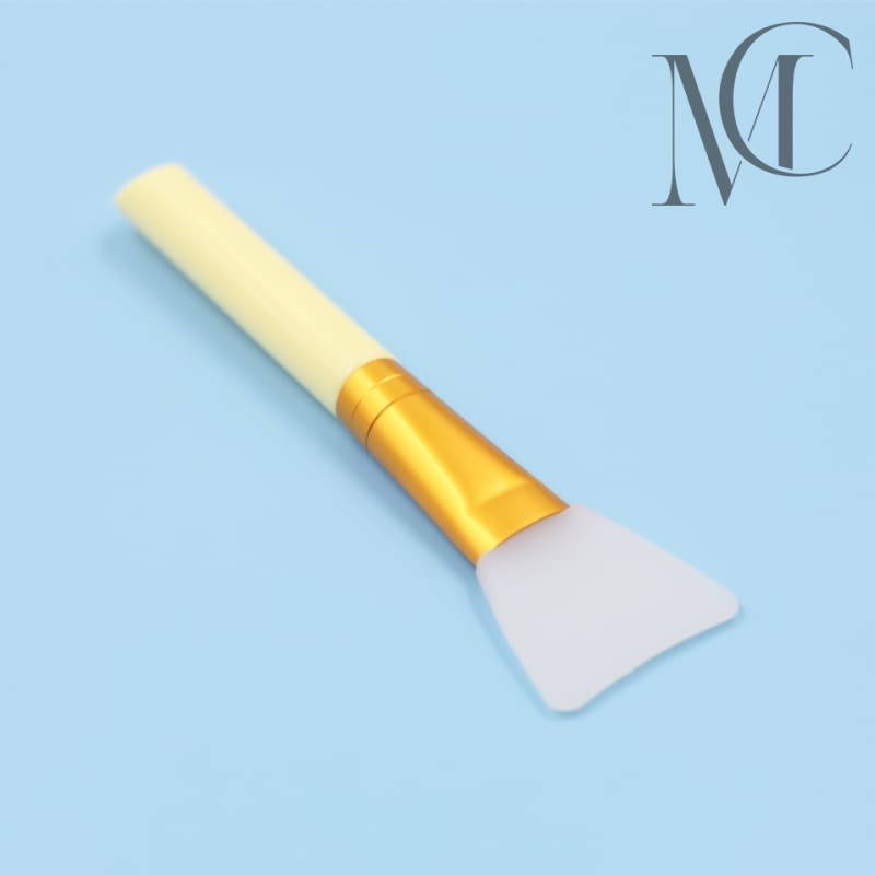 Mask Brush Manufacturer Silicone facial mask applicator brush with yellow handle and gold ferrule on a blue background.