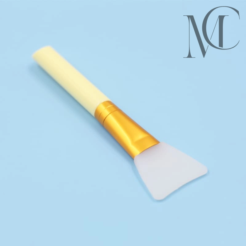 Fabricante de pinceles para mascarillas Pincel aplicador de mascarilla facial de silicona con mango amarillo y virola dorada sobre fondo azul.