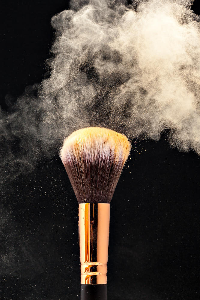 Makeup brush with gold powder dust against a black background.