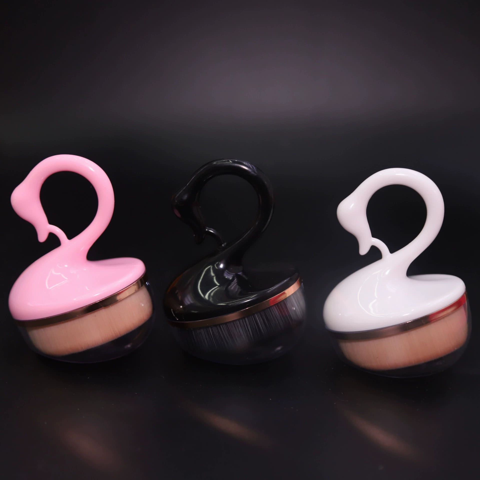 Three swan-shaped makeup brushes in pink, black, and white.