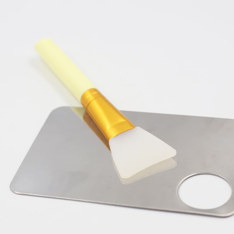 Silicone face mask brush on a stainless steel mixing palette.