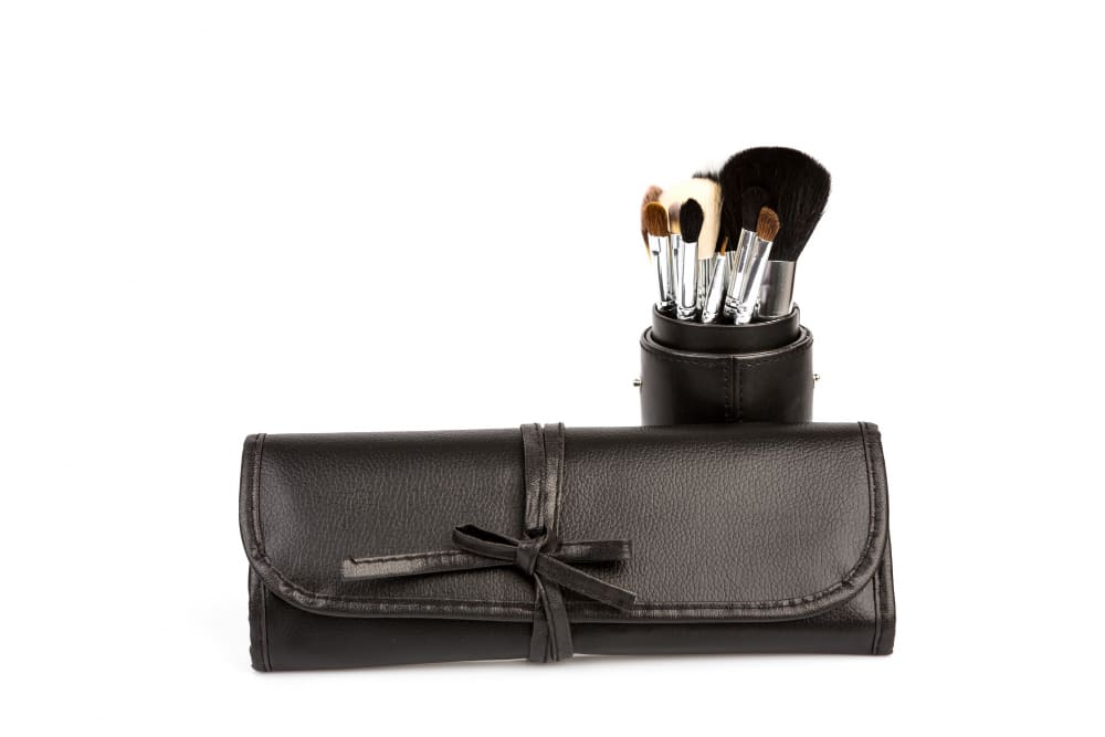 Estuche y vaso de cuero negro para brochas de maquillaje con brochas surtidas.