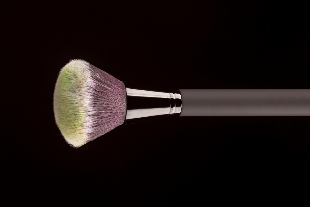 Close-up of a makeup brush Close-up of a makeup brush with green-tipped bristles against a black background.