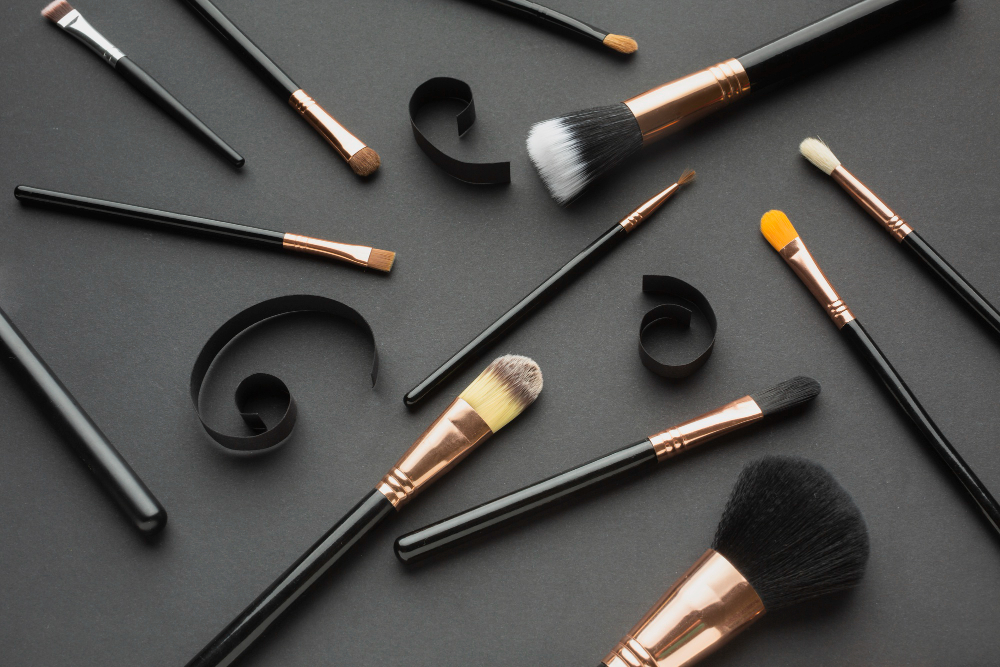 Assorted makeup brushes on a dark background with black paper curls.