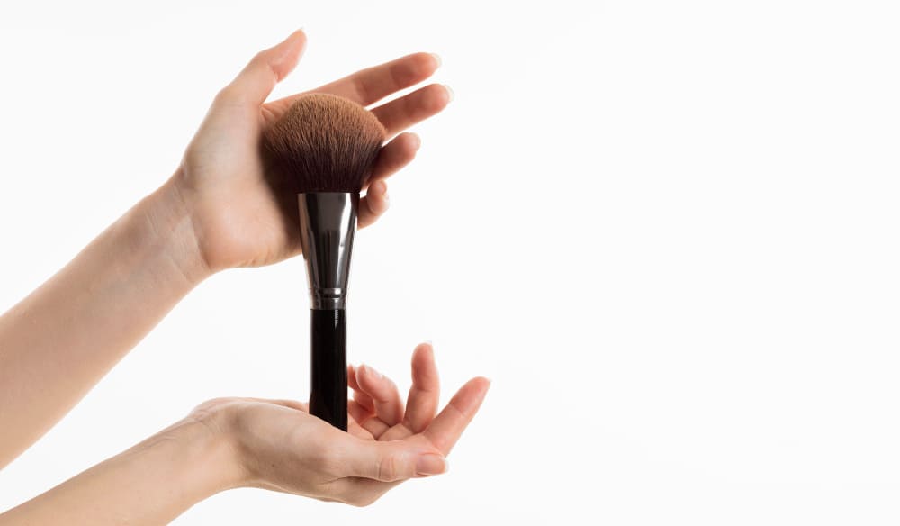 Hands holding a large makeup brush against a white background.