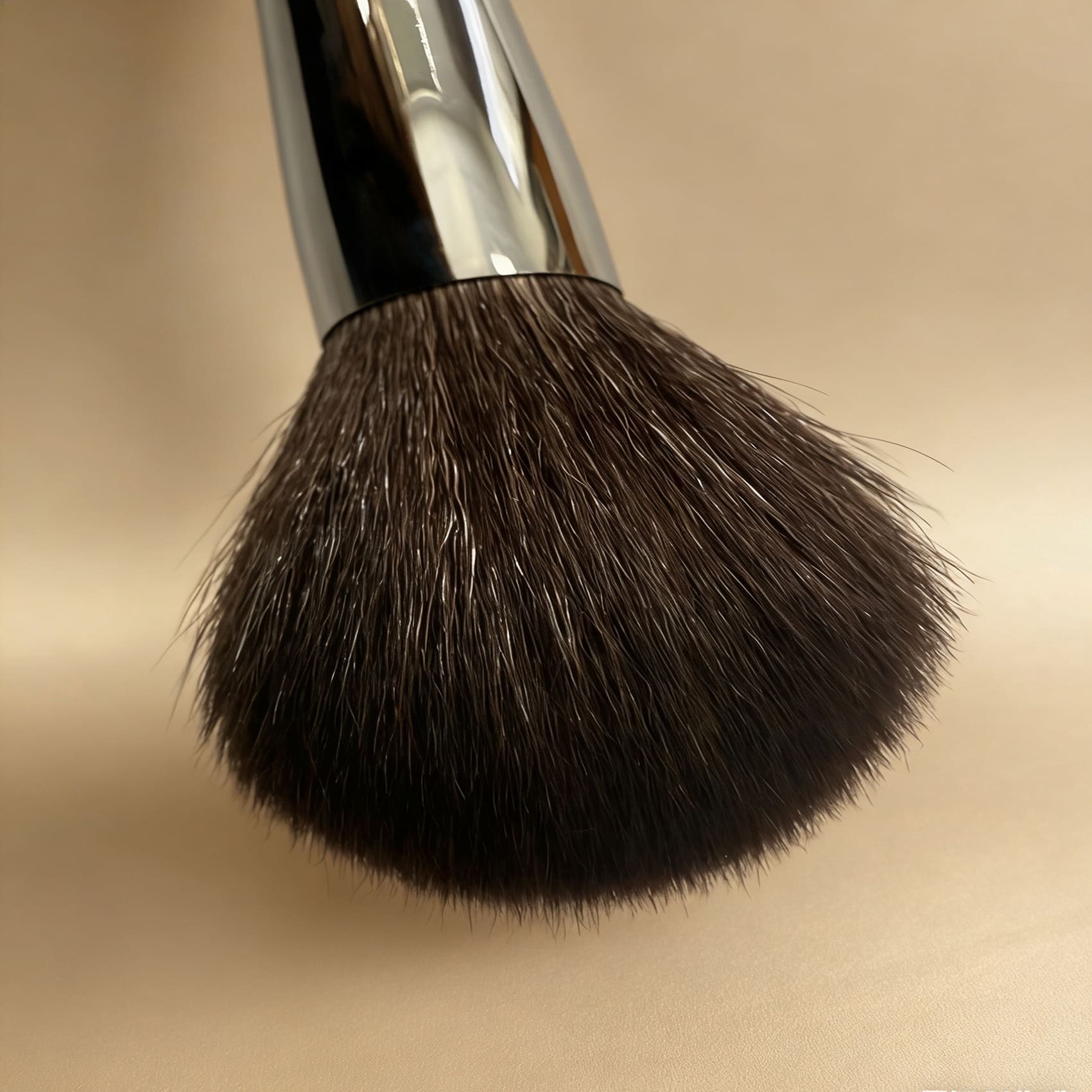 Close-up of a fluffy makeup brush with dark bristles and a silver handle.
