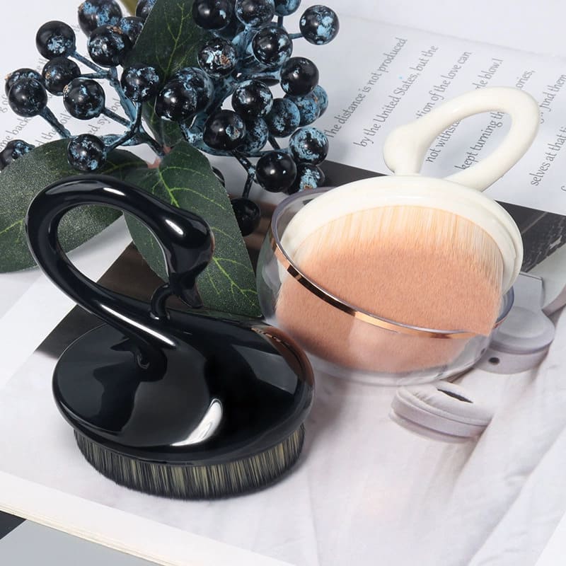 Close-up of a black swan-shaped powder brush and a beige powder brush on a magazine with berry accents.