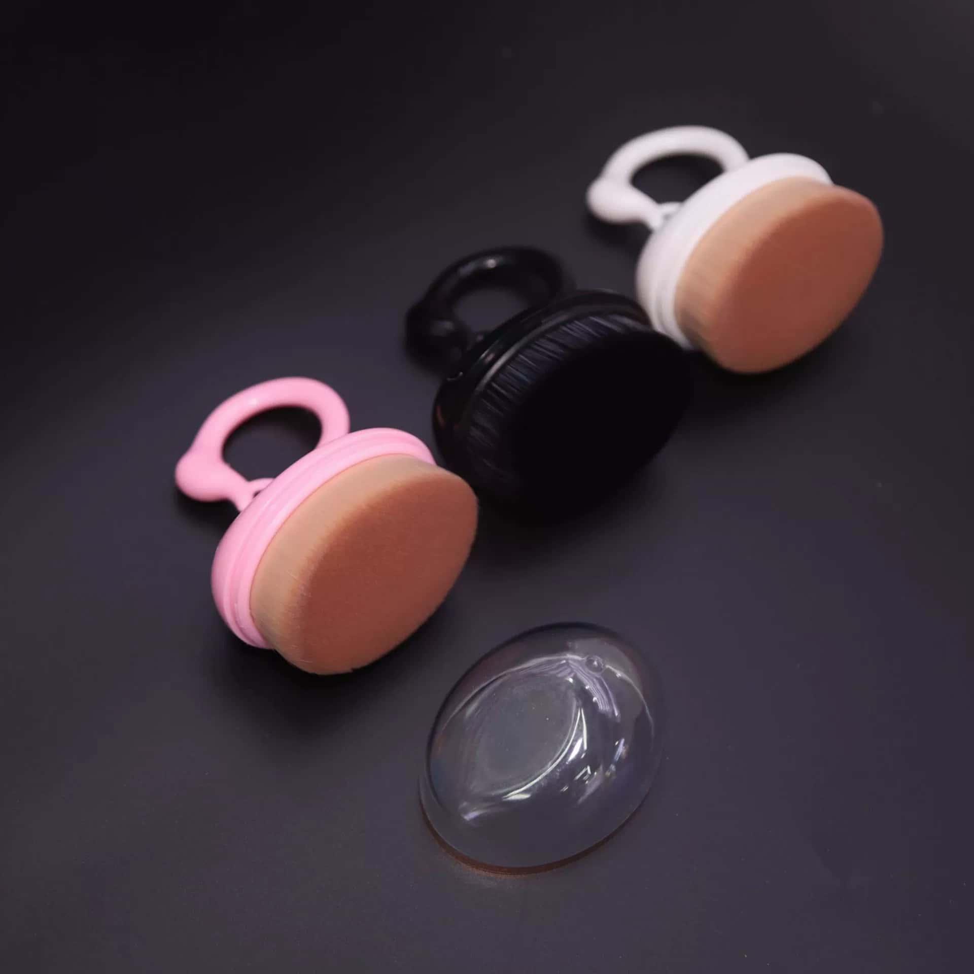 Makeup brushes with ring handles and a plastic storage cover on a black surface.