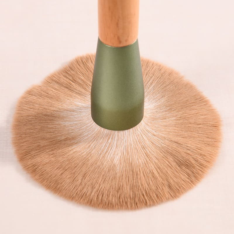 Close-up of a large, fluffy makeup brush with a wooden handle and green ferrule.