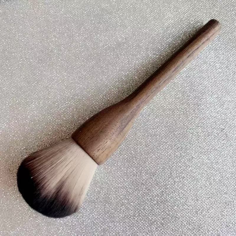 Makeup brush with a wooden handle and ombre bristles on a glittery surface.