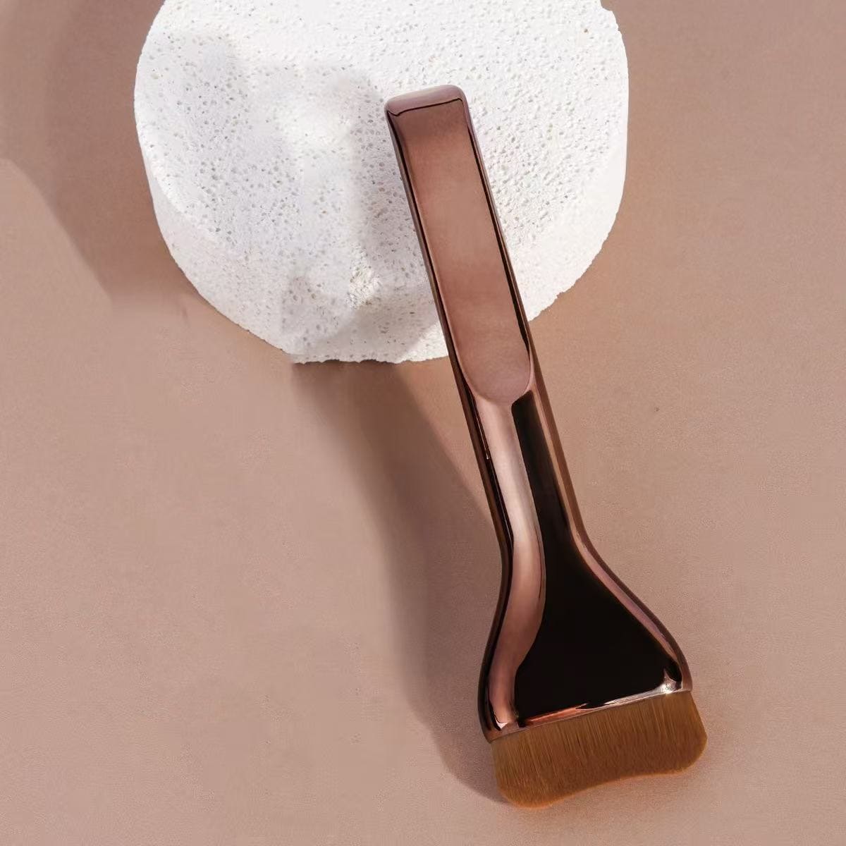 Rose gold facemask brush on a beige background.