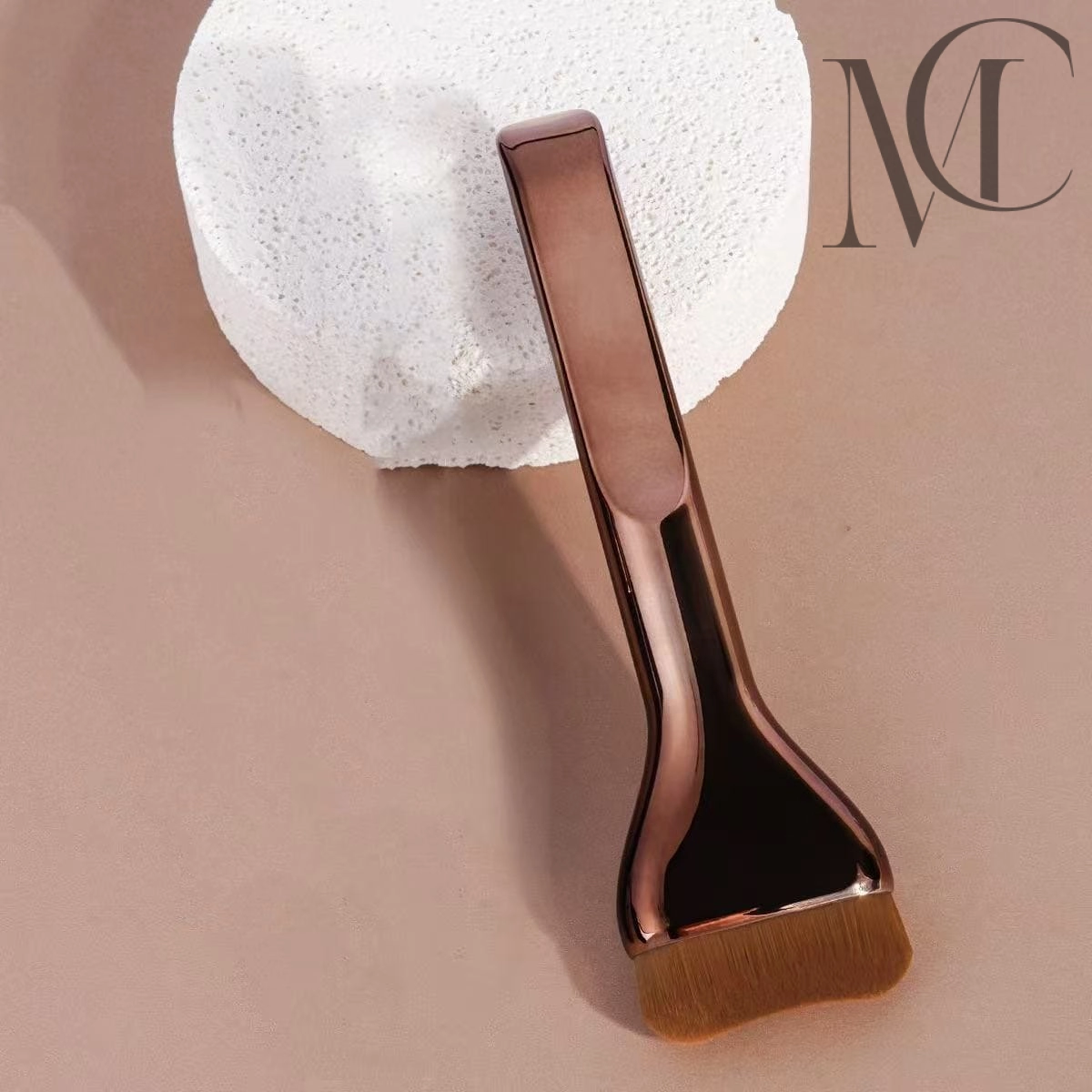 Brocha de base ondulada personalizada Pincel para mascarilla facial en color oro rosa sobre fondo beige.