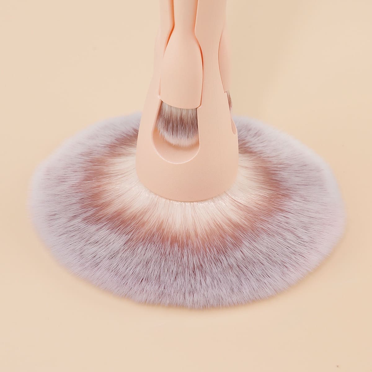 Close-up of a large makeup brush with light pink handle and white-tipped purple bristles.