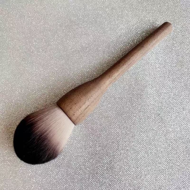 Makeup brush with wooden handle and two-toned bristles on a glittery silver background.