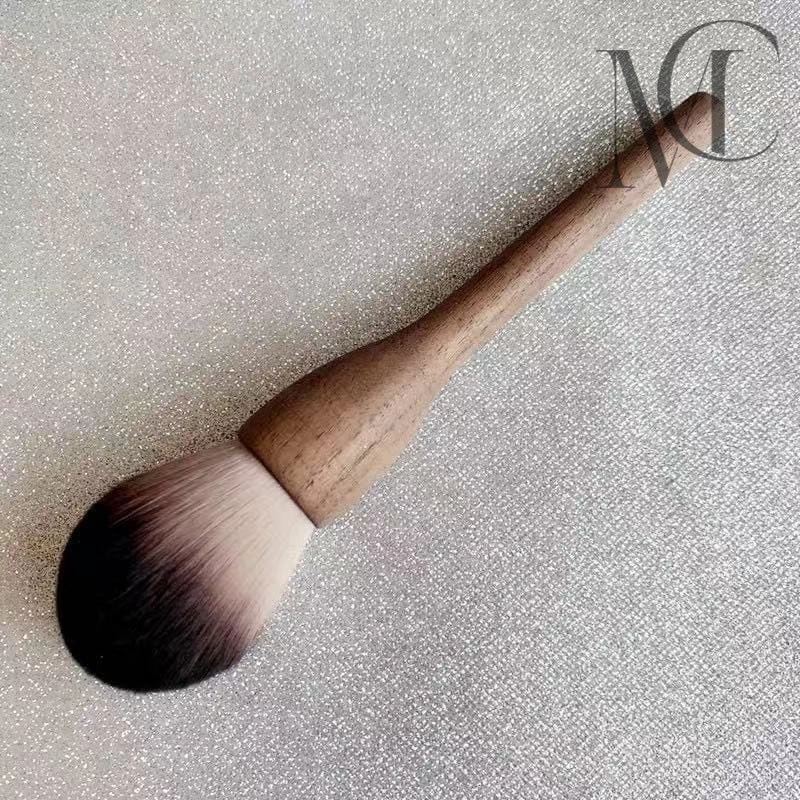 Eco-friendly makeup brush manufacturer Makeup brush with wooden handle and two-toned bristles on a glittery silver background.