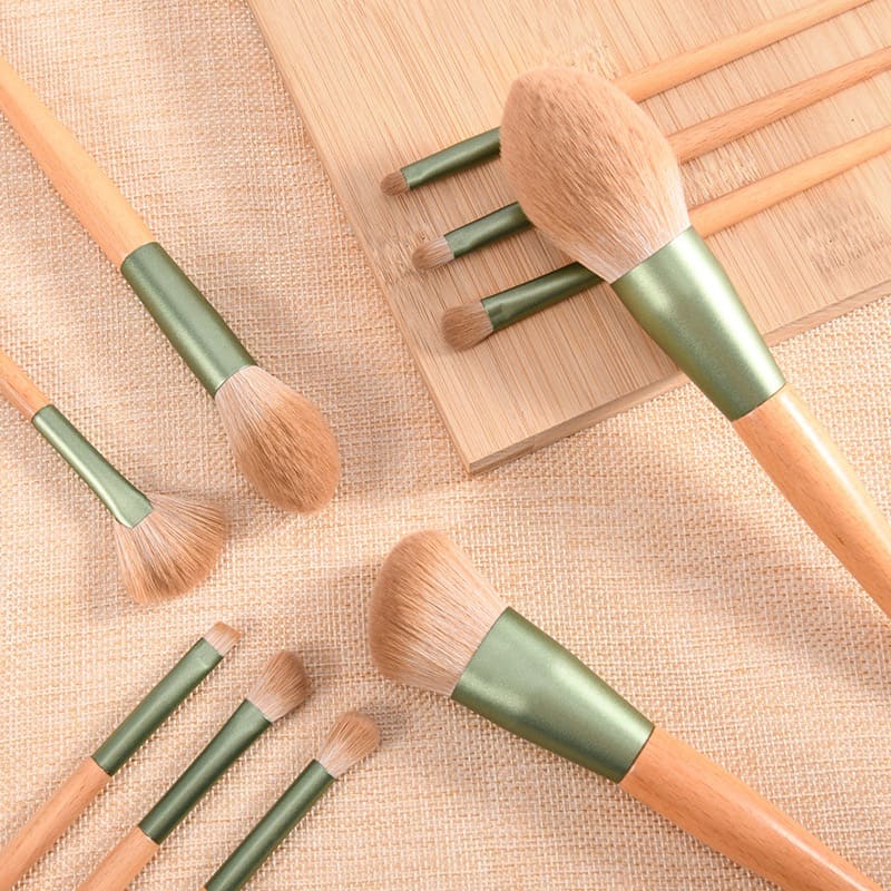 Makeup brushes with wooden handles and green ferrules on a textured surface.