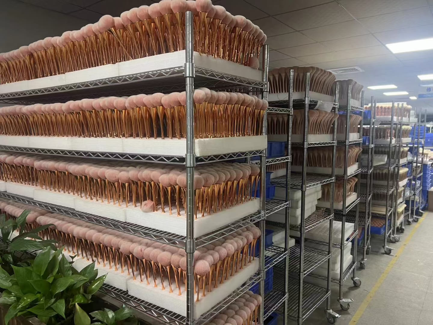 Shelving racks filled with rows of pink and gold makeup brushes in a factory.