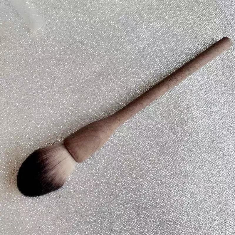 Makeup brush with a wooden handle on a glittery surface.