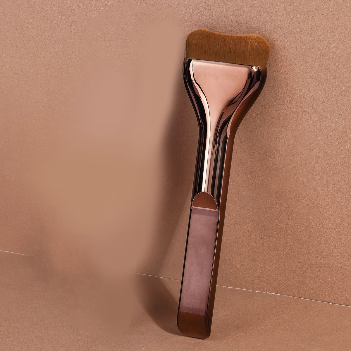 Rose gold foundation brush on a tan background.