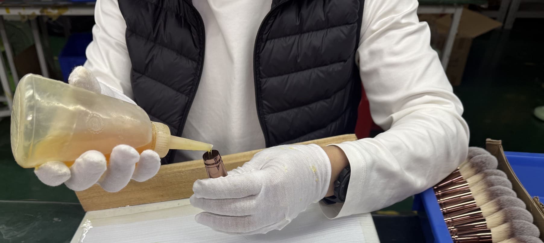 Worker wearing gloves applying glue to the ferrule of a makeup brush.