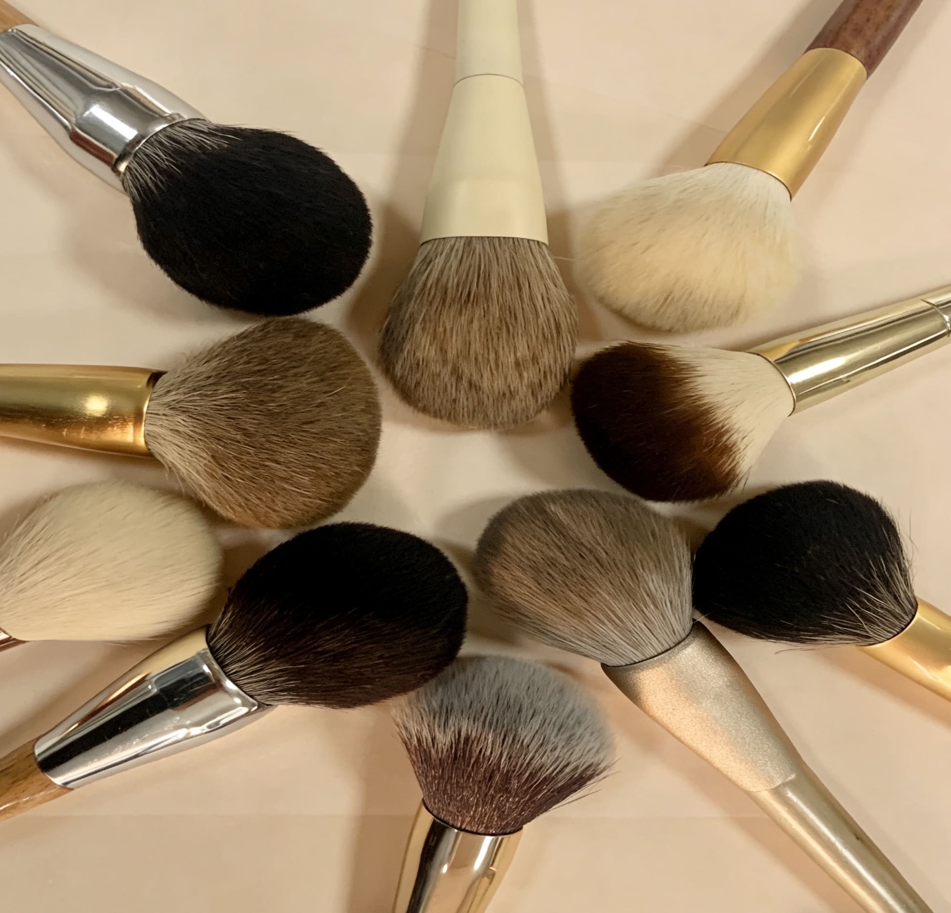 Collection of diverse makeup brushes arranged in a circular pattern on a light surface.