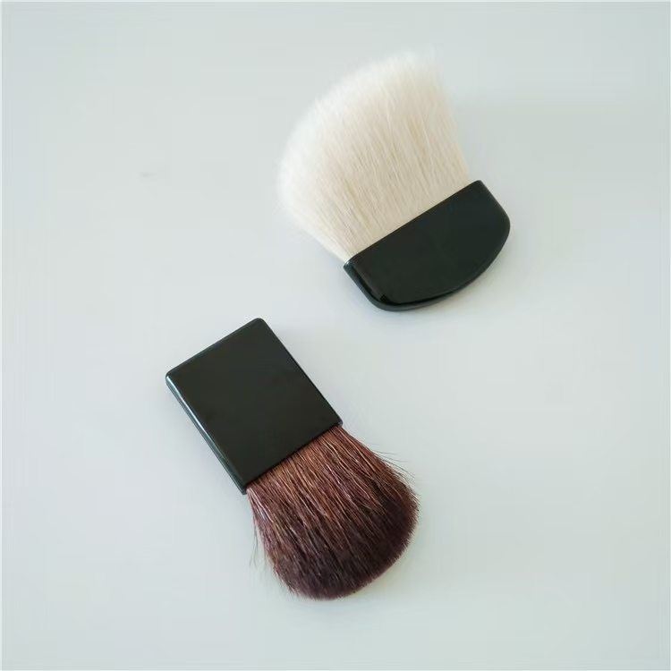 Two makeup brushes with black handles, one with white bristles and the other with brown bristles, on a white background.