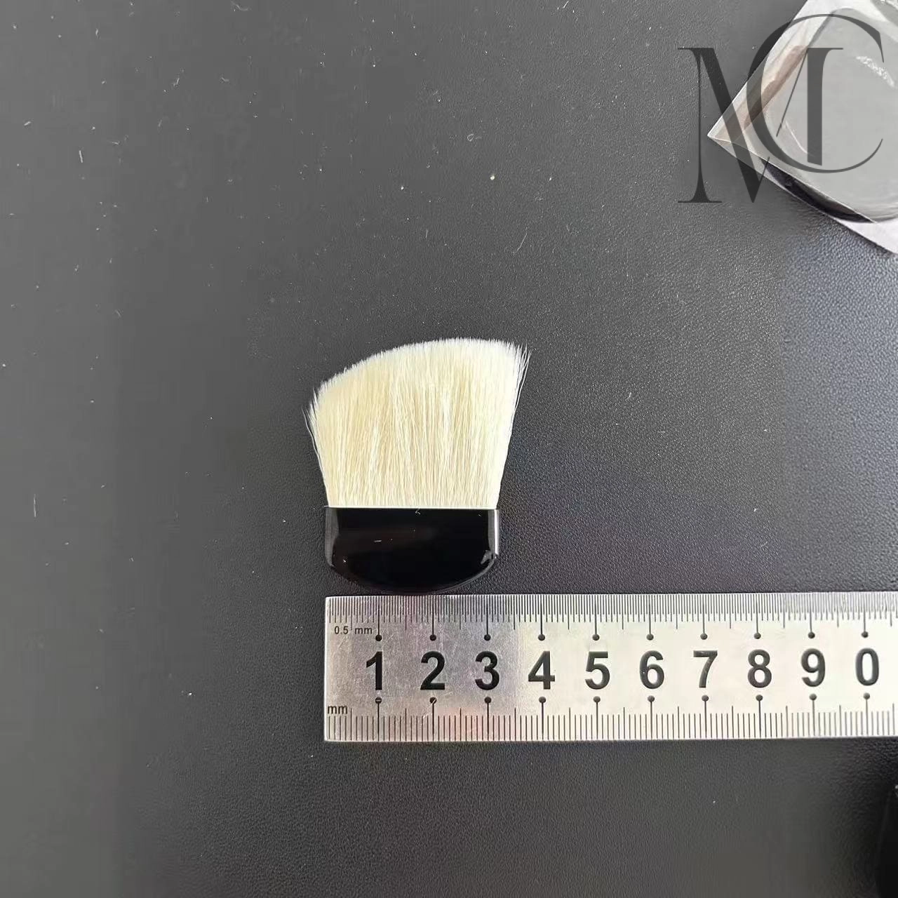 pinceau à poudre de marque privée Un pinceau de maquillage posé à côté d'une règle sur une surface noire.
