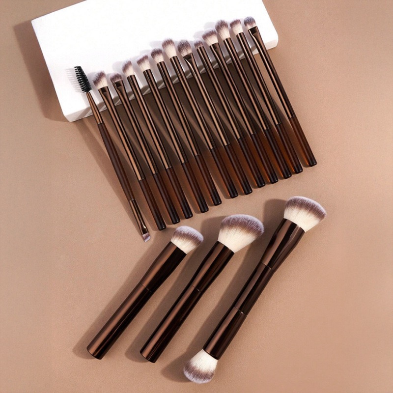 A collection of brown-handled makeup brushes of various sizes and shapes on a beige surface.