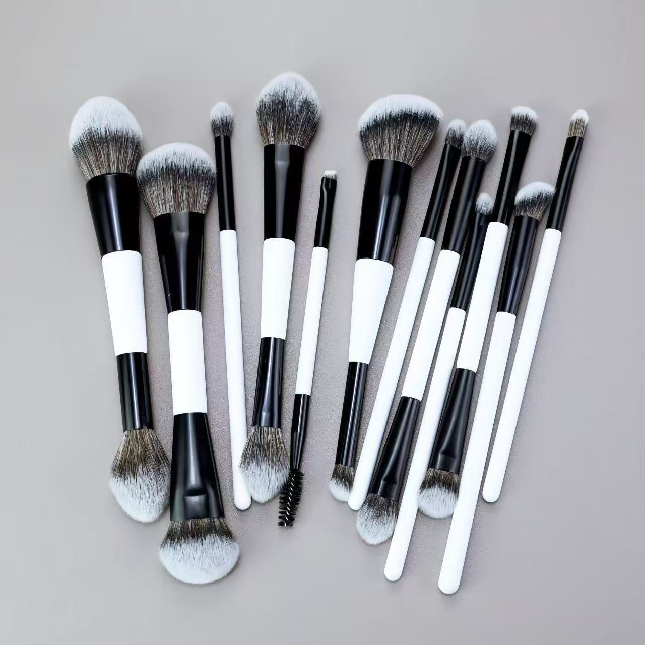 A collection of makeup brushes with black handles and white tips, arranged on a gray surface.
