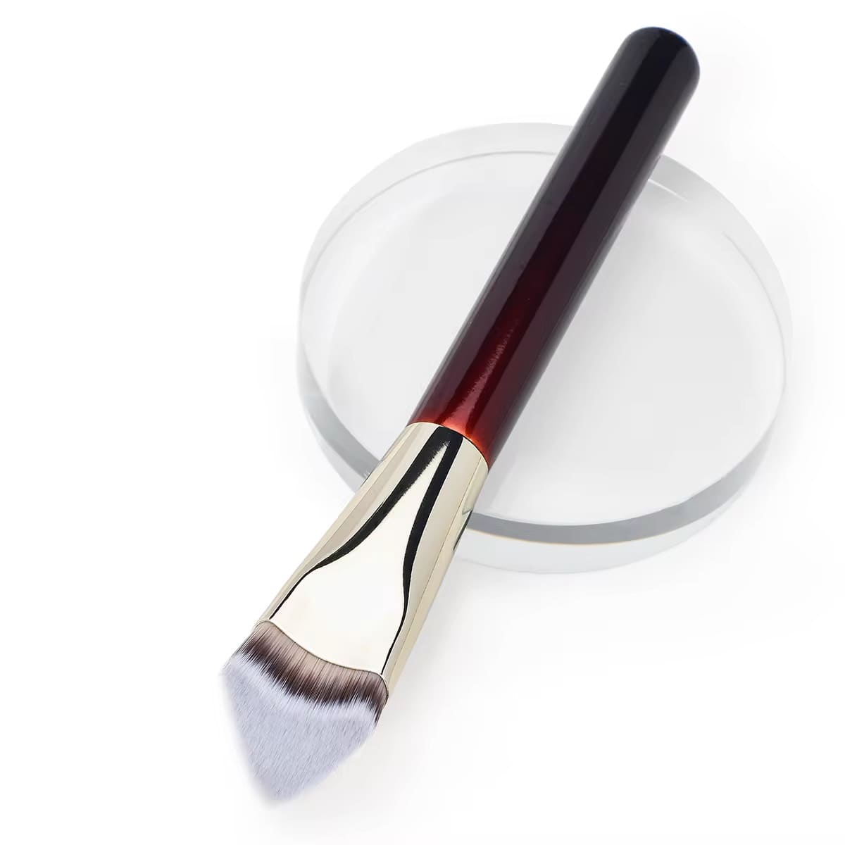Makeup brush with dark red handle and angled light bristles on a clear stand.