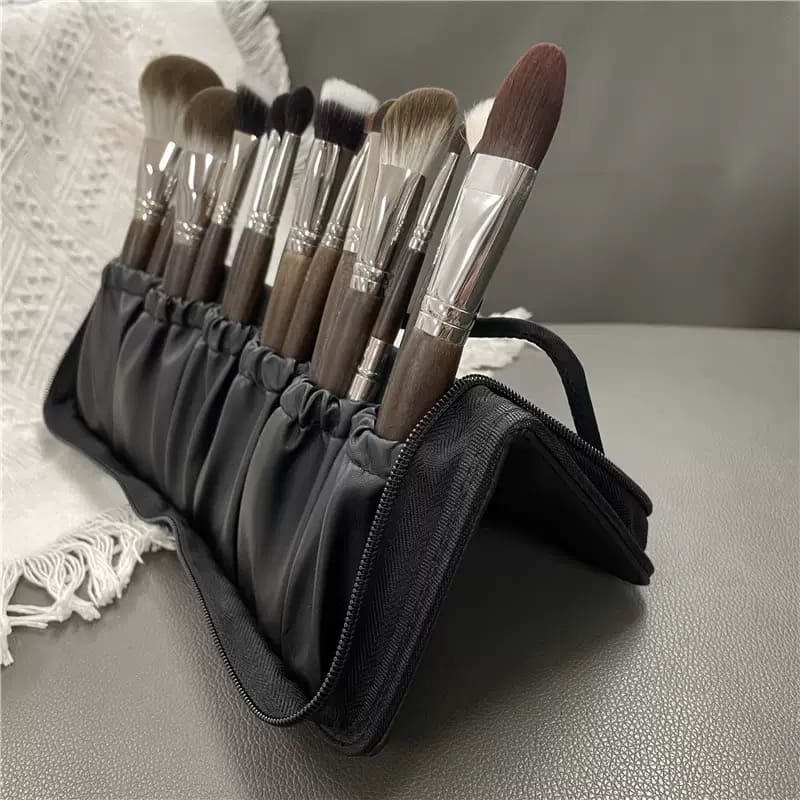 Juego de brochas de maquillaje con mangos de madera oscura y virolas plateadas en un estuche enrollable negro.