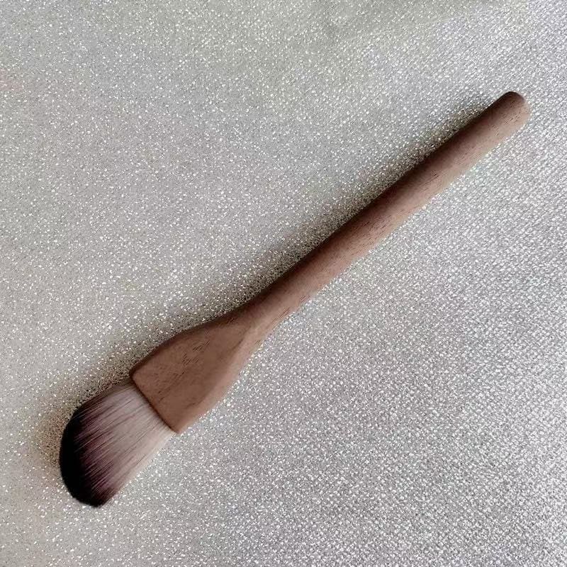 Makeup brush with wooden handle on a glittery surface.
